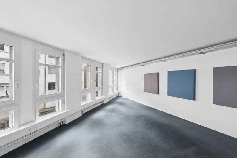 Empty room with white walls, blue carpet, large windows, three paintings on the wall