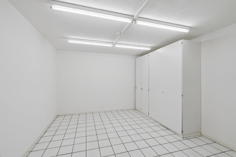 Empty room with white walls, white tiled floor, white cabinets, and fluorescent ceiling lights