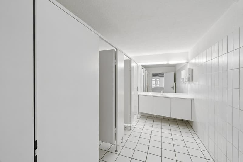 Bathroom with white tiles, white cabinets, sink, mirror, and toilet stalls