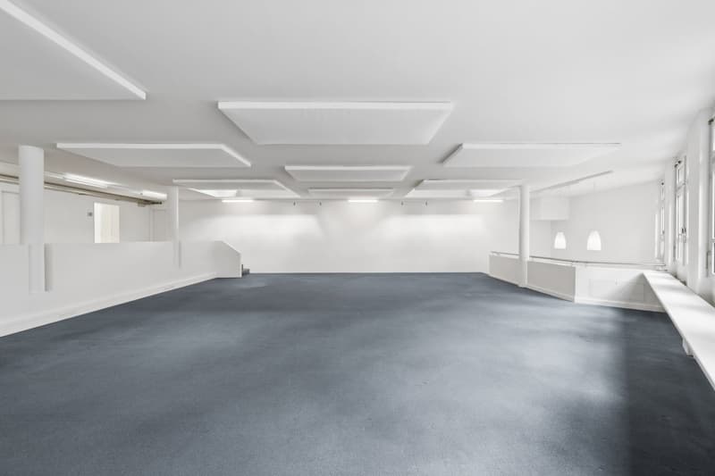 Empty room with white walls, gray floor, white ceiling with recessed lighting, white pillars, and white benches.