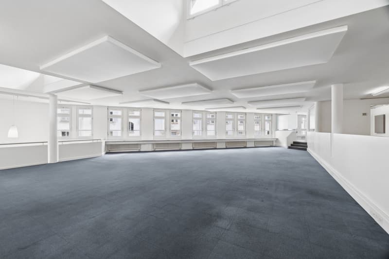 Empty room, white walls, gray floor, large windows, high ceiling, white pillars, white ceiling panels, white radiators