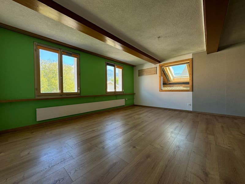 Spacious room with green walls, wooden floors, and large windows providing natural light. The room has a clean and minimalist design with a bench or seating area along the wall.