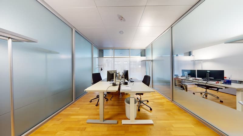 modern office room with glass walls, wooden floor, desks with monitors, office chairs