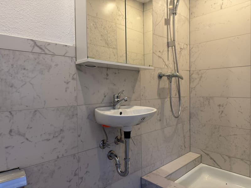 bathroom with white sink, glass shower enclosure, white marble tiles, silver shower head, mirror above sink