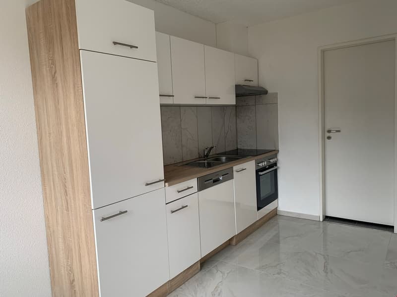 Modern kitchen with white cabinets, wood countertop, built-in dishwasher, and gray marble-like tile flooring.