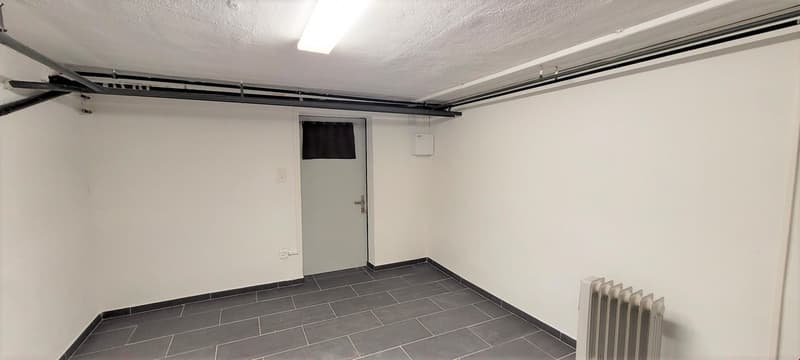 Empty room with white walls, gray tiles, a door, and a radiator