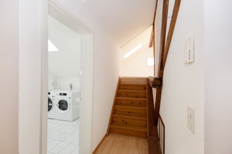 Laundry room with washing machine and dryer, wooden stairs, white walls, white tiles