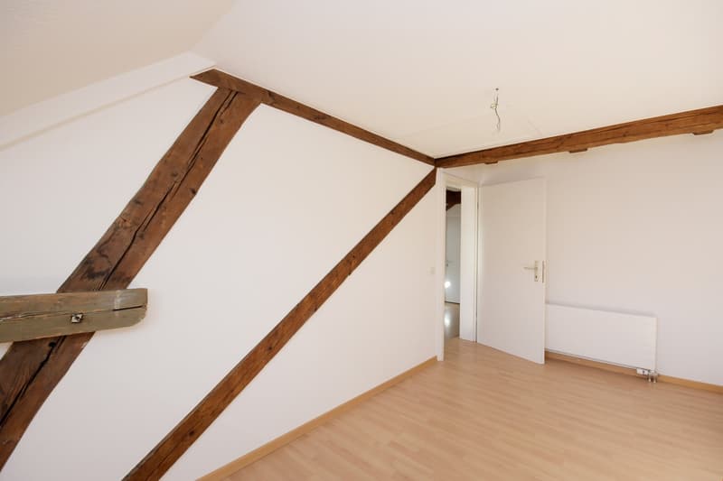empty room, wooden beams, white walls, wooden floor, open door, radiator