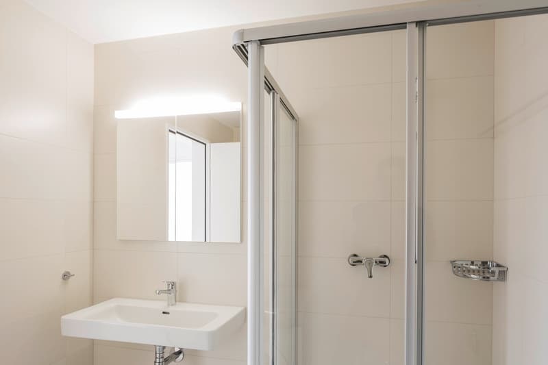 Bathroom with white tiles, white sink, mirror, shower enclosure, and a soap dish.