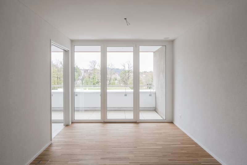 empty room, wooden floor, white walls, large glass doors, balcony, view of trees and buildings