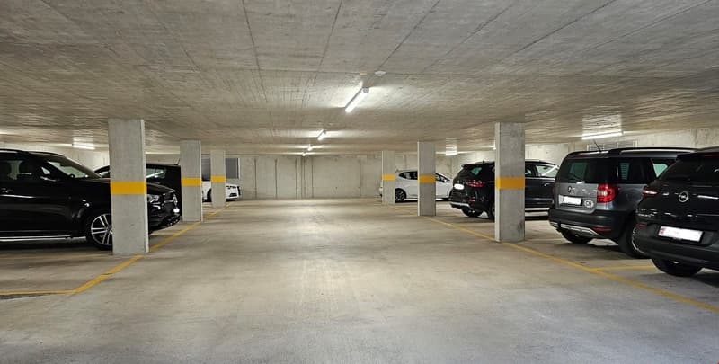 Empty underground parking lot with concrete pillars and yellow markings. Several cars parked in the lot.