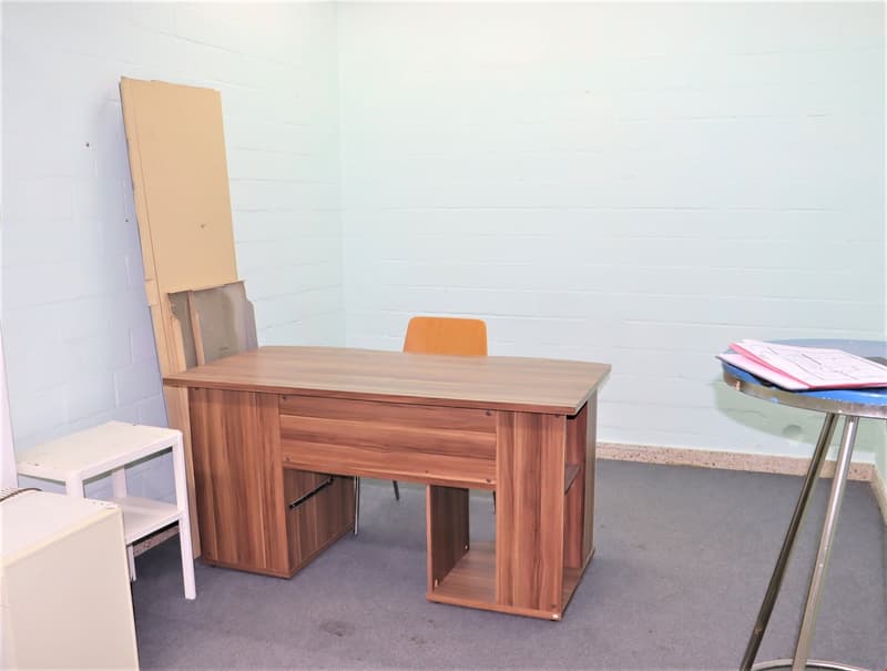 The image shows a simple office setup with a wooden desk, an orange chair, and some other office supplies and furniture in the background.