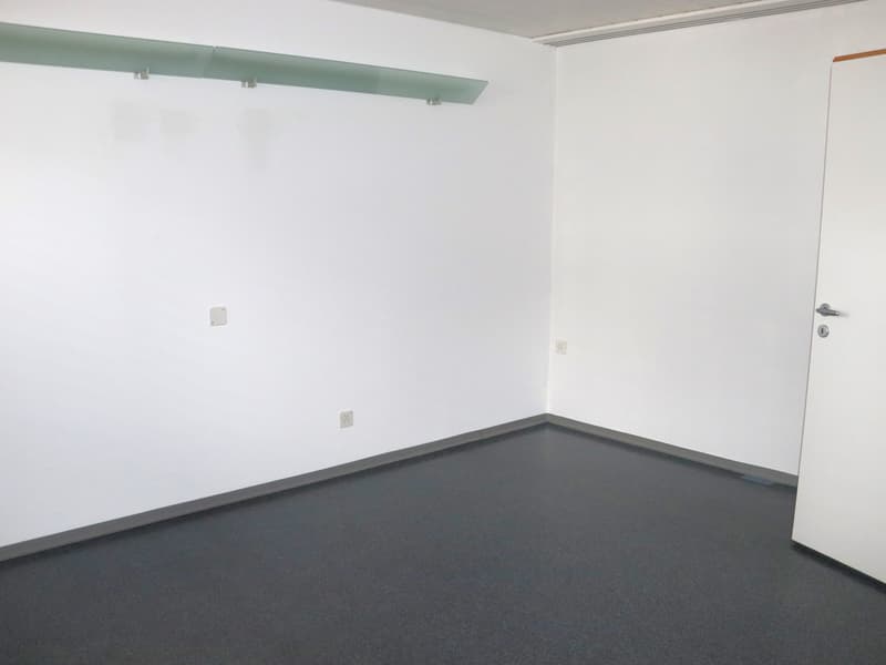 empty room with white walls, gray floor, mounted shelf, power outlets, and an open door