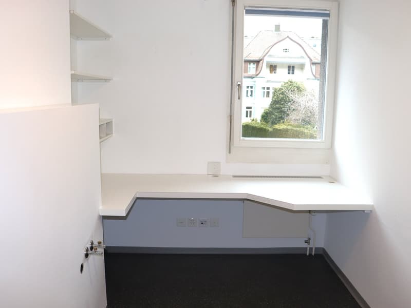 white desk, three electrical outlets, glass window, white walls