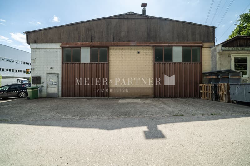 2-story commercial building with a brown wooden exterior, large windows, and a sign that says 'MEIER & PARTNER IMMOBILIEN' on the front facade. The building appears to be used for a real estate company or office space.