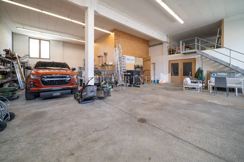 Large open garage space with concrete floor, storage shelves, ladders, and an orange Isuzu vehicle parked inside.