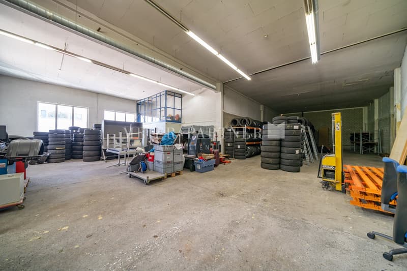 Large industrial warehouse space with concrete floor, shelving units, stacked tires, and various equipment and supplies.