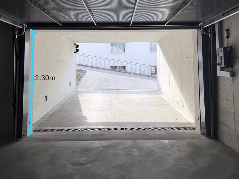 Empty concrete garage, measuring 2.30m in height, with automatic sliding doors, a concrete floor, and drainage system.