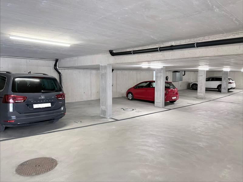 Parking space, concrete ceiling, cars parked, pipes on ceiling, lighting on ceiling