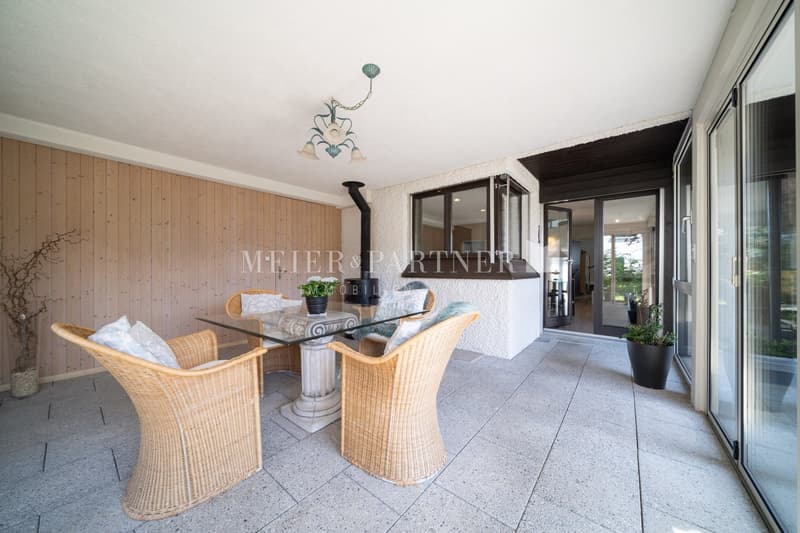 4 wicker chairs, glass dining table, potted plants, chandelier, wooden wall, sliding glass door, outside view