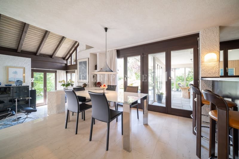 Modern dining room with glass dining table, modern chairs, and large sliding doors opening to a balcony. A large cabinet, white floor, and warm lighting create a cozy atmosphere.
