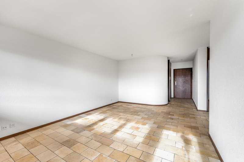 Empty room with white walls, tiled floor, power outlets, wooden door.