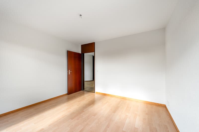 Empty room with white walls, wooden floor, open door, mirror