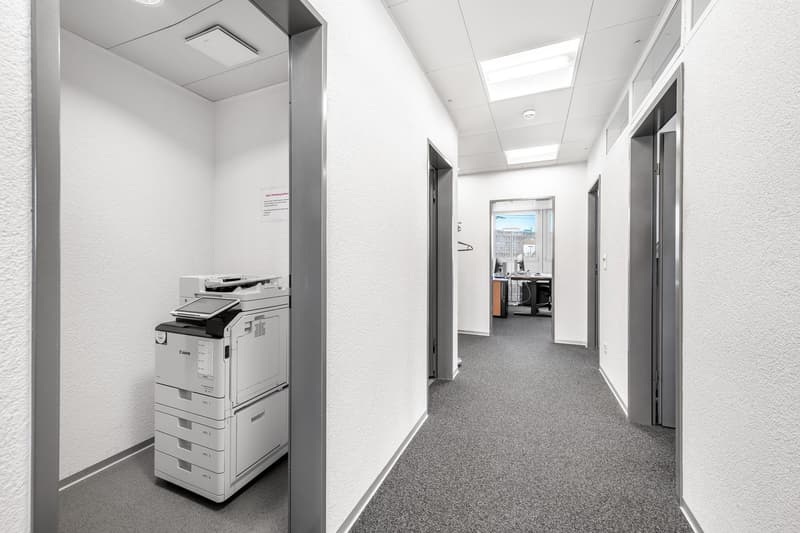 An empty office room with a printer on the left and open doors on the right.