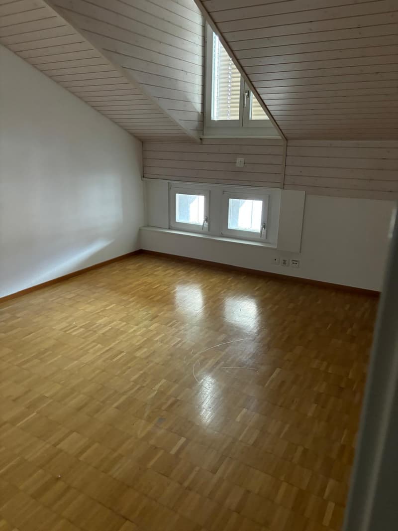 Attic bedroom with slanted wooden ceiling, hardwood floor, and two small windows