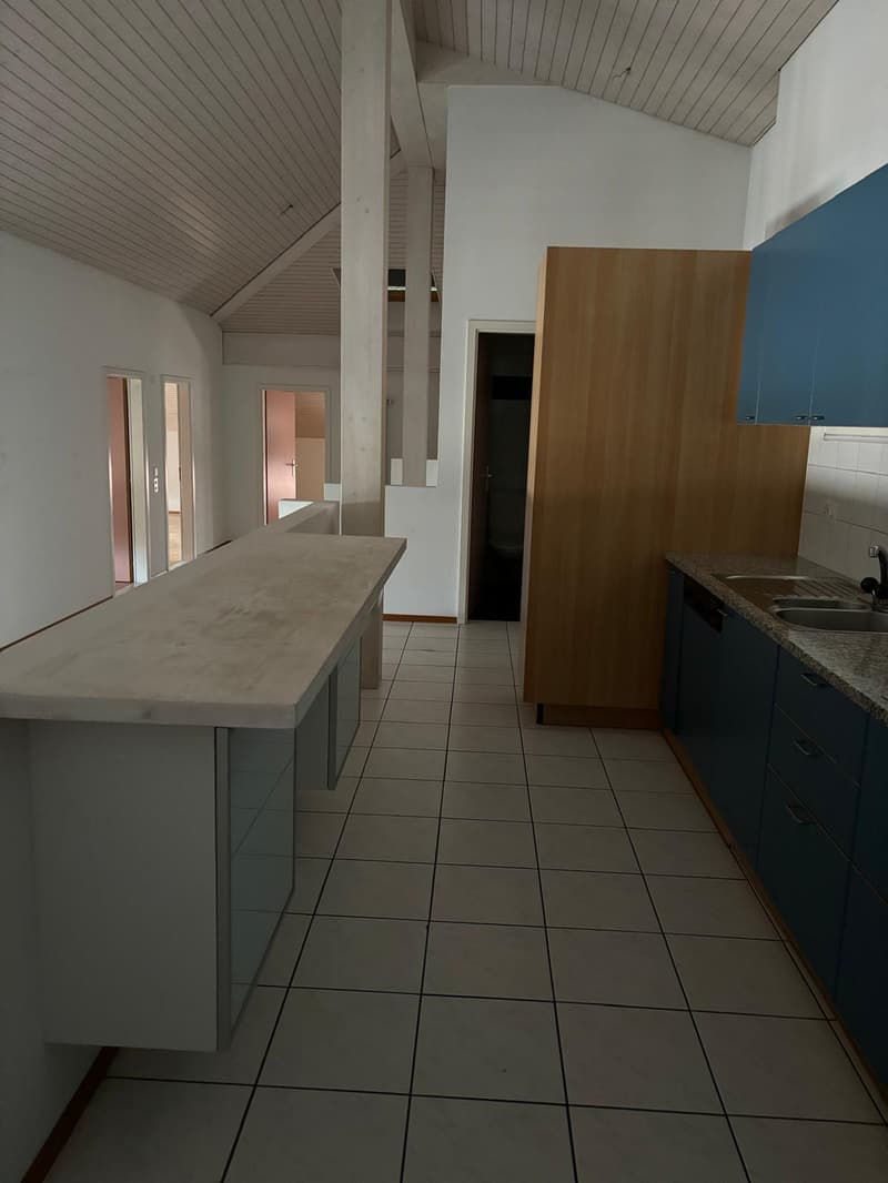 Spacious kitchen with concrete countertop, wooden cabinets, and tiled flooring. A dishwasher is visible in the kitchen.