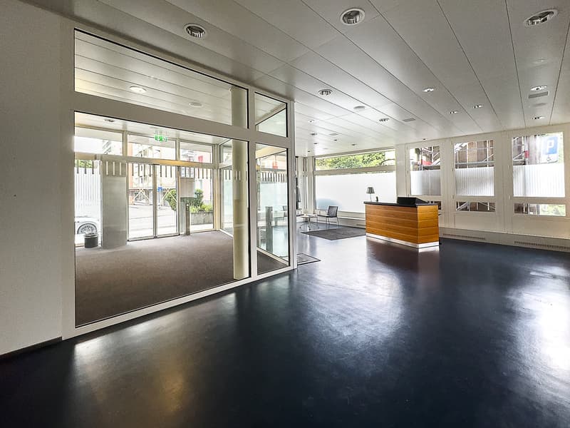 spacious lobby, large glass doors, reception desk, wooden pillars, black flooring, modern lighting fixtures