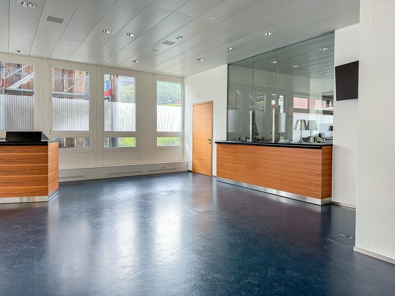 Open office space, white walls, wooden floors, multiple windows, glass partition wall, wooden reception desks, ceiling mounted lighting