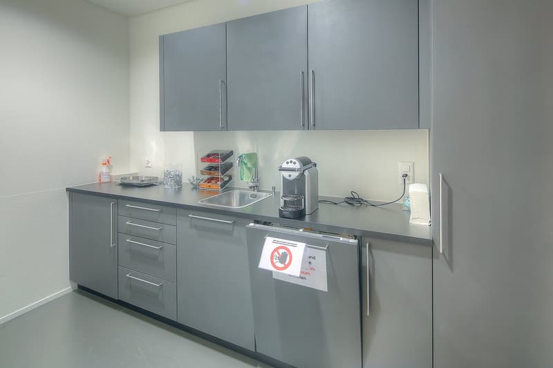 Modern kitchen with gray cabinets, stainless steel appliances including a dishwasher, sink, and countertop space with various kitchen items