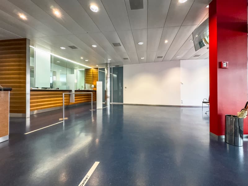 Empty hall, wooden counter, glass panels, modern lighting fixtures, red pillar, white floor, a chair, a fire extinguisher, a trash can