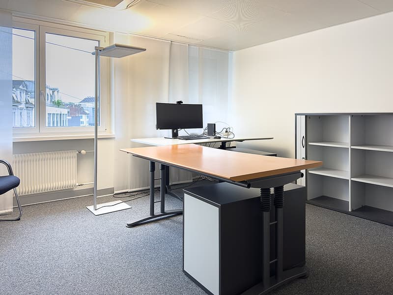 A room with a desk, monitor, keyboard, mouse, radiator, and ceiling lamp