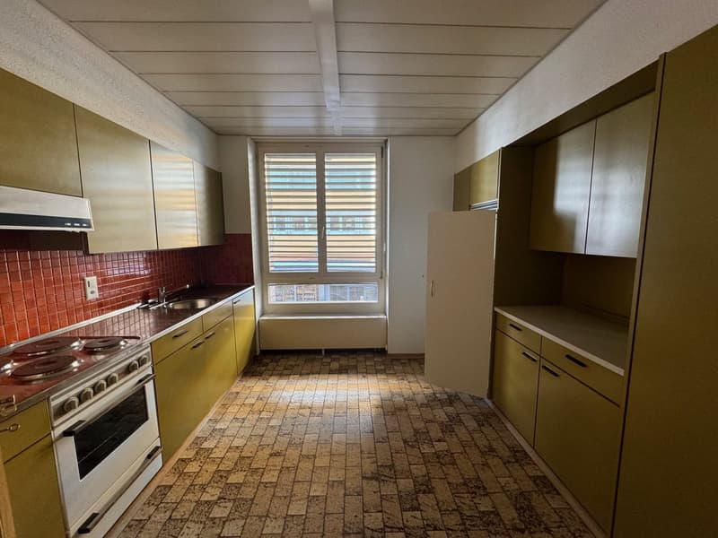 Tiled floor, yellow cabinetry, stove with oven, sink, window with shutters, ceiling lamp