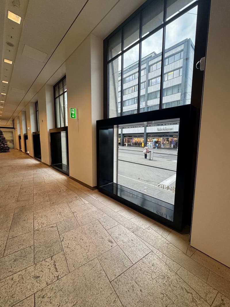 Empty hallway with tiled floor, large glass windows, exit sign, view of a street and a building