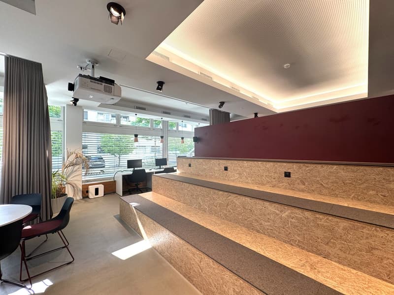 The image shows a modern office space with a reception area. The reception desk is made of wood panels and has a sleek, minimalist design. There are computers and other office equipment visible in the background, indicating this is a workspace. The room h