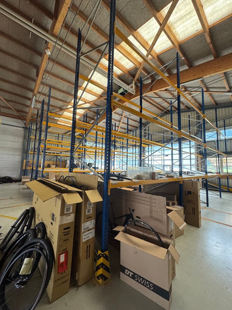 Warehouse with high shelves, multiple storage boxes, bicycles, steel beams, and windows