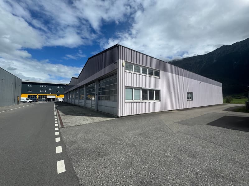 Large building with slanted roof, many windows, flat terrain, mountains in background