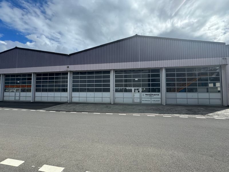 Large industrial building, glass doors, white walls, empty parking space in front, Velohans sign