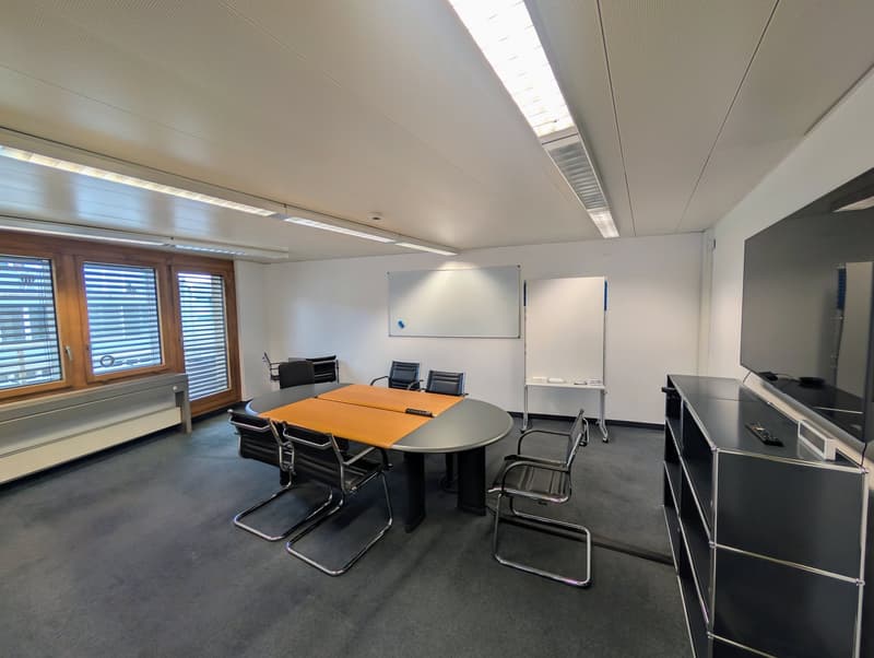 empty meeting room with a round table, chairs, whiteboard, TV, and windows