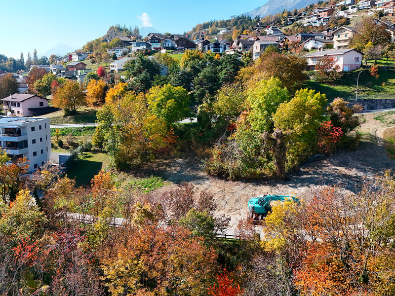 Aerial view of a hillside with several houses, one under construction, surrounded by trees and greenery.