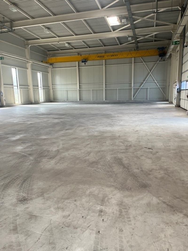 Large open warehouse space with concrete floor, metal framing, and an overhead crane visible.