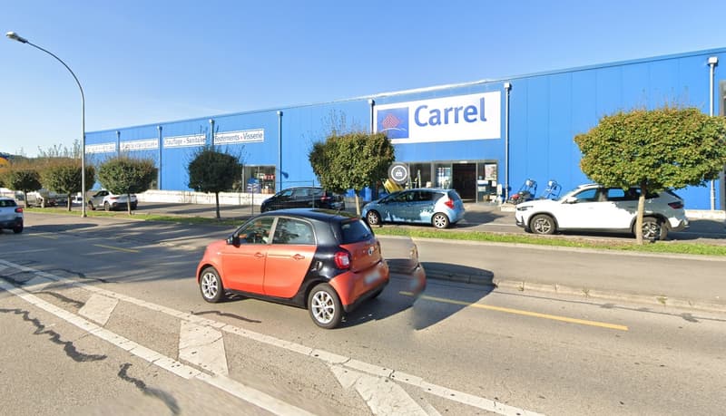 A large blue building with the Carrel logo, surrounded by a parking lot with several cars parked in front of the store.