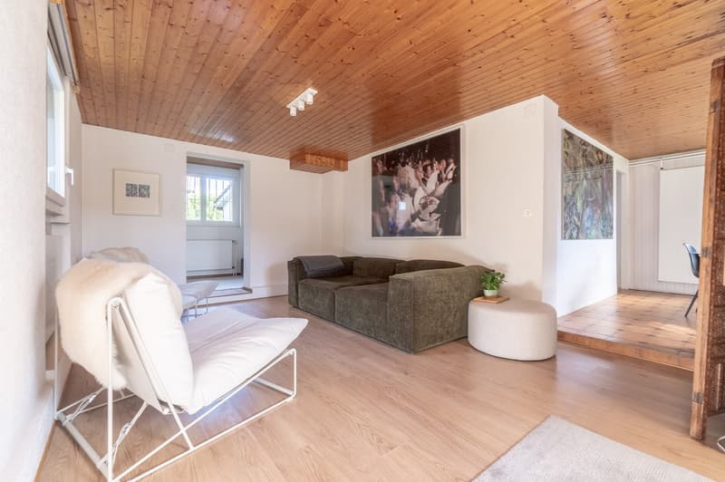 modern living room with hardwood floors, white walls, wooden ceiling, sofa, chairs, side table, paintings on the wall, a potted plant, radiator