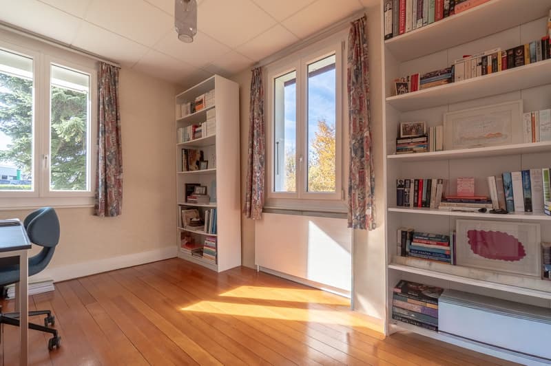 room with wooden floor, bookshelves, desk, office chair, windows, radiator