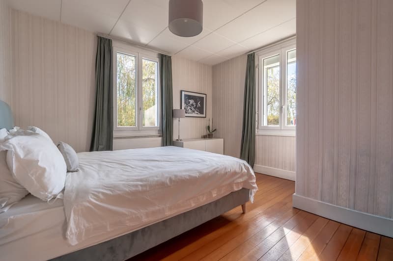 bedroom with wooden floor, double bed, nightstand, picture frame, lamp, white and grey walls, large windows, curtains