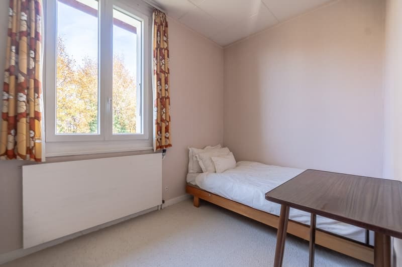 Small bedroom with bed, desk, window, curtain and heater