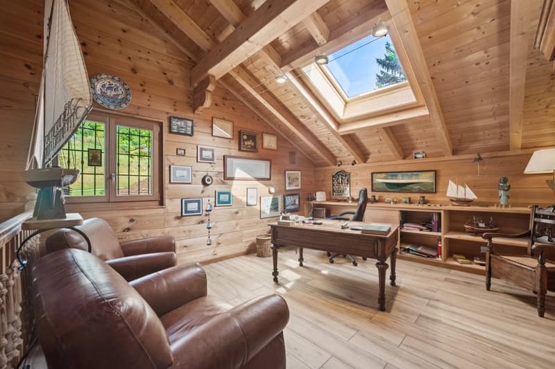 small attic room with wood walls, skylight, office desk, shelves, armchairs, sailboat sculpture